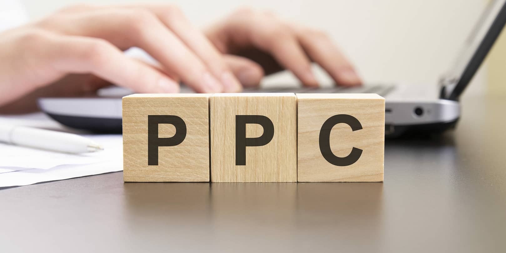 Ppc Acronym From Wooden Blocks With Letters. Background Hands On A Laptop With Blur. Business Concept.